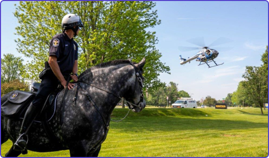Male police officer sitting on a horse in a park with a police helicopter taking off in the background